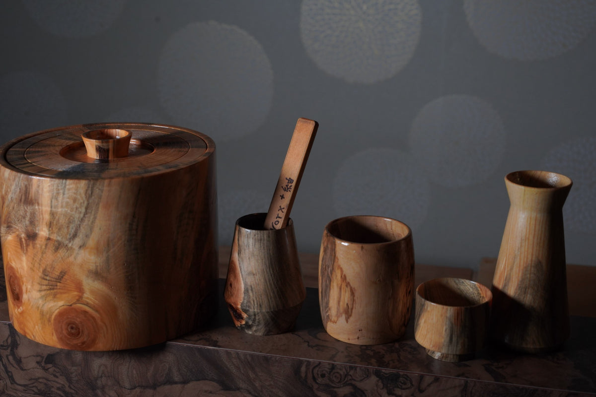 Turned wooden ice bucket, cups and a sake flask on a marble ledge