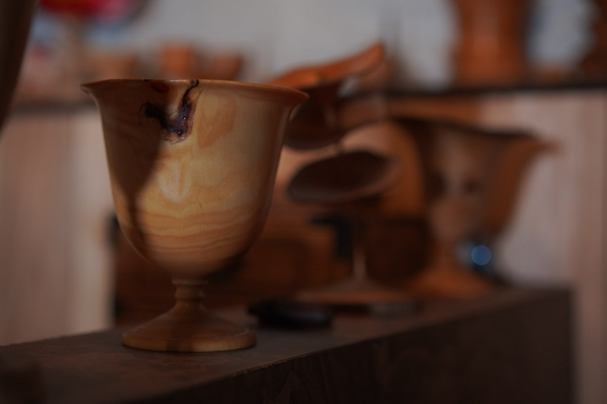 A pale turned goblet on a workshop shelf, other pieces behind it